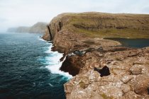 Wanderer sitzt auf Felswand und blickt auf Ozean, Feroe-Inseln — Stockfoto