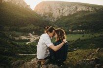 Coppia carina abbracciare e dure fronti mentre seduto sul pendio roccioso sullo sfondo di bella valle e montagne — Foto stock