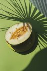 Halbe Melone auf Teller auf grünem Hintergrund mit Schatten von Palmblättern — Stockfoto