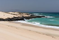 Oceano litoral com ondas de água azul e areia com rochas com montanhas nebulosas, Ilhas Canárias — Fotografia de Stock