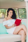 Lächelnde junge Frau sitzt im Wohnwagen und liest Buch — Stockfoto
