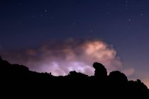 Промені і хмари в нічний шторм над горою під зоряним небом — стокове фото