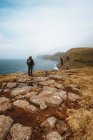 Caminante irreconocible de pie en la costa con palo y mirando al océano en las Islas Feroe - foto de stock