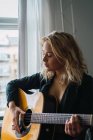 Blonde junge Frau spielt zu Hause Gitarre — Stockfoto