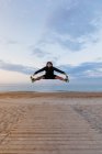 Активний чоловік у спортивному одязі високо стрибає під час тренування на відкритому повітрі на піщаному пляжі — стокове фото