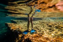 Jambes de garçon portant des palmes debout sur la pierre sous l'eau de mer — Photo de stock