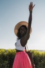 Модная афроамериканка в шляпе с чемоданом и прогулкой по сельской дороге летом — стоковое фото