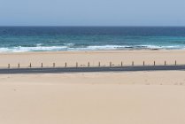 Огороженная автомагистраль на песчаной равнине с побережьем с бесконечным голубым волнистым океаном, Канарские острова — стоковое фото