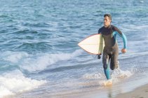 Masculino fazendo alguma corrida na praia antes de surfar . — Fotografia de Stock