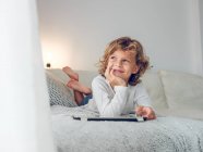Веселый мальчик лежит с цифровой табличкой на диване и смотрит в сторону — стоковое фото