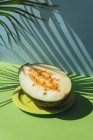 Halbe Melone auf Teller auf blauem und grünem Hintergrund mit Schatten von Palmblättern — Stockfoto