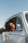 Щаслива молода чорна жінка в стильних сонцезахисних окулярах дивиться з вікна автомобіля насолоджуючись літнім сонячним світлом — стокове фото