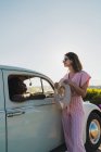 Elegante bruna in occhiali da sole appoggiata sulla macchina all'esterno e parlando con una bella donna nera all'interno in estate luce solare brillante — Foto stock