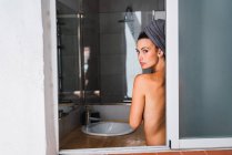 Молодий топлес жінку, що стоїть у ванній кімнаті з рушником на голову — стокове фото