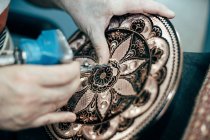 Обрезание рук неузнаваемого мастера, делающего гравировку на тарелке — стоковое фото