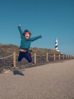 Cheerful cute boy having fun and jumping on background of beacon tower. — Stock Photo