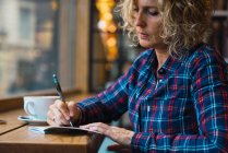 Frau sitzt im Café und schreibt in Notizbuch — Stockfoto