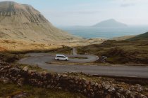 Weißes Auto fährt auf Serpentinenstraße in den Bergen auf Feroe Islands — Stockfoto