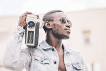 Black man in sunglasses walking with vintage radio device — Stock Photo