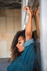 Junge afrikanisch-amerikanische Frau mit lockigem Haar im Jeanshemd lehnt sich mit erhobenen Händen und geschlossenen Augen an die Wand — Stockfoto