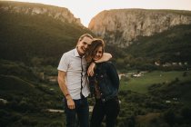 Cute couple hugging and toughing foreheads while standing on background of beautiful valley and mountains — Stock Photo