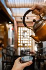 Рука урожая наливая воду из медного чайника в чашку во время восточной чайной церемонии — стоковое фото