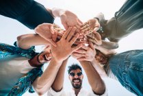 From below shot of young friends laughing and holding hands together while standing on background of clear sky — Stock Photo