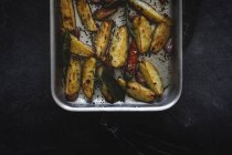 Roasted golden crunchy potato wedges in baking pan on black surface — Stock Photo