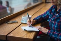 Mulher sentada no café e escrevendo em caderno — Fotografia de Stock