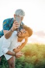 Guapo barbudo chico dando paseo a cuestas a alegre novio y posando para selfie mientras pasar tiempo en la naturaleza juntos - foto de stock
