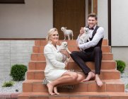 Excited bride and groom with little white Chihuahua dogs sitting on steps of porch and smiling at camera — Stock Photo