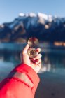 Human dressed in red jacket holding golden compass in sunny day on blurred Canadian mountains background — Stock Photo