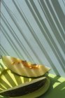 Ломтики свежей дыни на голубом и зеленом фоне с тенями пальмовых листьев — стоковое фото