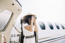 Viajero femenino de pie cerca del avión y tomando fotos - foto de stock