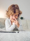 Fröhlicher Junge liegt mit digitalem Tablet auf Couch und pickt Nase — Stockfoto