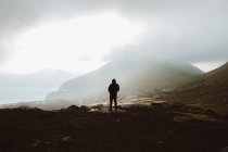Unrecognizable hiker man standing on coast under clouds and looking at ocean on Feroe Islands — Stock Photo