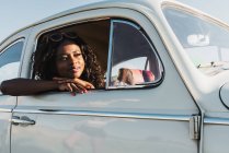 Heureuse jeune femme noire dans des lunettes de soleil élégantes regardant par la fenêtre de la voiture profitant de la lumière du soleil d'été — Photo de stock