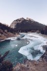 Fluss fließt in geschmolzenem Hochlandsee an schneebedeckter Felsspalte mit braunen Felsen und wenigen Wintertannen an sonnigen Tagen — Stockfoto