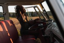 Mulher afro-americana encantadora sorrindo e olhando para longe através da janela do carro vintage, enquanto passa o tempo na natureza no dia ensolarado — Fotografia de Stock