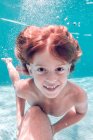 Bambino dai capelli rossi che si tuffa in acqua e guarda la fotocamera sullo sfondo di acqua trasparente — Foto stock