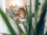 Смеющийся мальчик с планшета на диване дома — стоковое фото