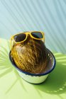 Fresh melon with sunglasses in bowl on blue and green background with shadows of palm leaves — Stock Photo