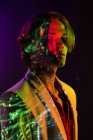 Привабливий андрогінний чоловік тримає очі закритими, стоячи під барвистим освітленням у темній кімнаті — стокове фото