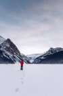 Blick aus der Ferne auf einen anonymen Reisenden, der in einem weitläufigen kalten, schneebedeckten Feld mit felsigen, dunklen Bergen im Hintergrund steht — Stockfoto