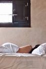 Vue arrière de la brune seins nus femme dormir dans le lit recouvert de drap de lit blanc sur le fond de la fenêtre avec la lumière du soleil entrant — Photo de stock