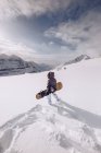 Unerkennbare Frau in warmer Kleidung und Snowboard mit Spezialmunition, die bergab gleitet? auf bewölktem Himmel Hintergrund — Stockfoto
