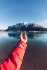 Human dressed in red jacket holding golden compass in sunny day on blurred Canadian mountains background — Stock Photo