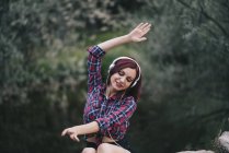 Red haired girl listens to music by the river — Stock Photo