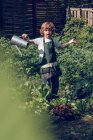Porträt eines Jungen mit lockigem Haar in Schürze, der Pflanzen im Garten gießt — Stockfoto