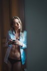 Thoughtful blonde woman in lingerie and shirt relaxing with cup at home — Stock Photo